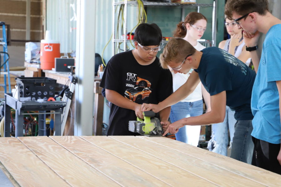 Lead designer junior Rhett Marazetta helps volunteer freshman Daniel Rogers cut siding with a circular saw.